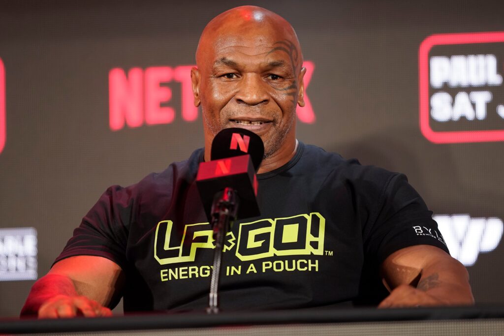 Mike Tyson engaged in a podcast recording with vibrant backdrop.