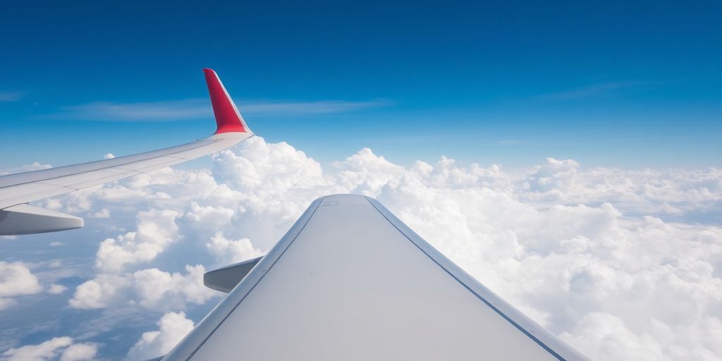 Airplane wing above turbulent clouds in a blue sky.