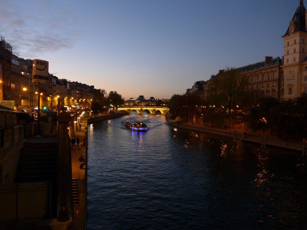 An illuminated Seine river cruise boat heading towards the Pont Neuf in Paris at dusk