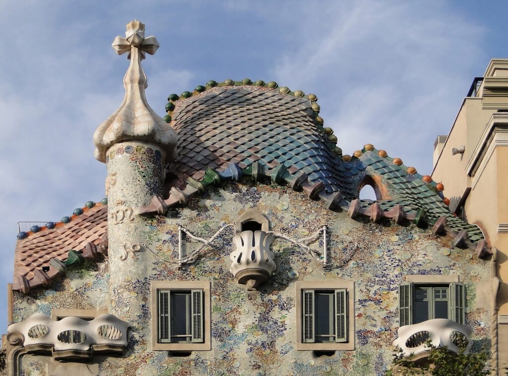 Bovenste deel van de gevel van Casa Batlló in Barcelona met het dak vol drakenschubben, de toren met kruis en de botachtige balkons