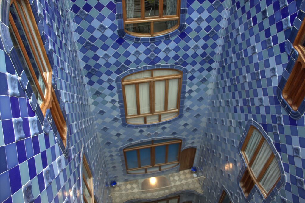 Blue-tiled light well inside Casa Batlló with wavy wooden windows