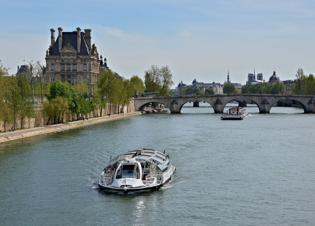 Een Batobus-boot en een rondvaartboot op de Seine naast het Louvre, met de Notre-Dame in de verte