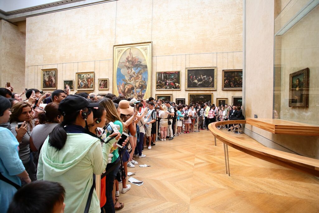 Menigte bezoekers die de Mona Lisa achter een hek fotografeert in de Salle des États van het Louvre
