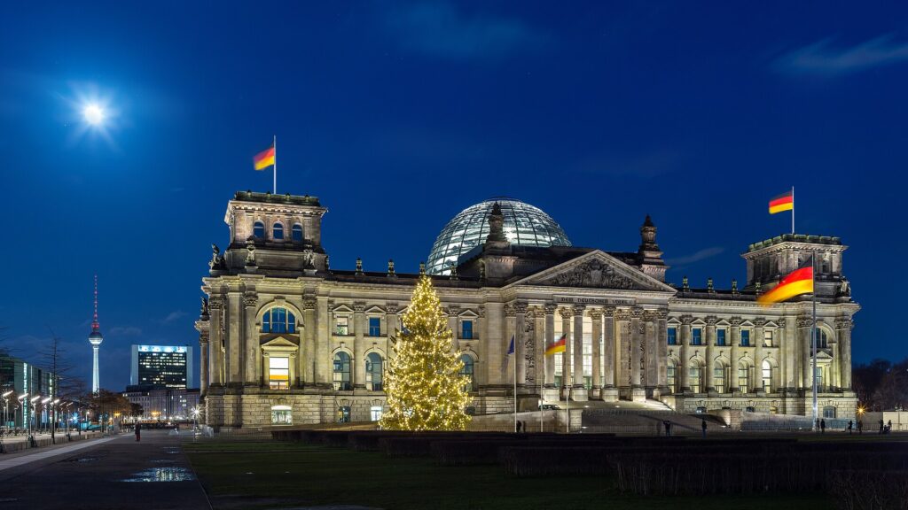 The Reichstag building with its glass dome at night, with the Berlin TV Tower in the distance