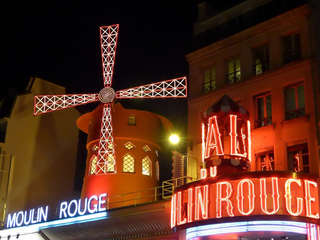 The illuminated red windmill and neon sign of the Moulin Rouge cabaret on boulevard de Clichy in Paris at night