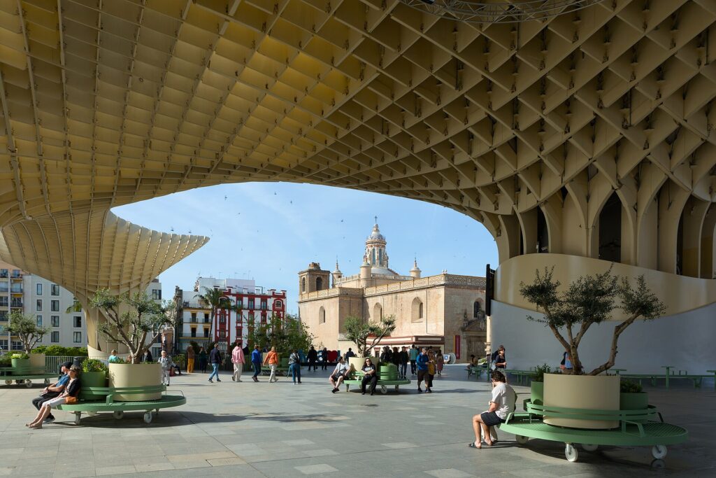 Das hölzerne Dach Metropol Parasol über der Plaza de la Encarnación in Sevilla, dahinter eine Kirchenkuppel