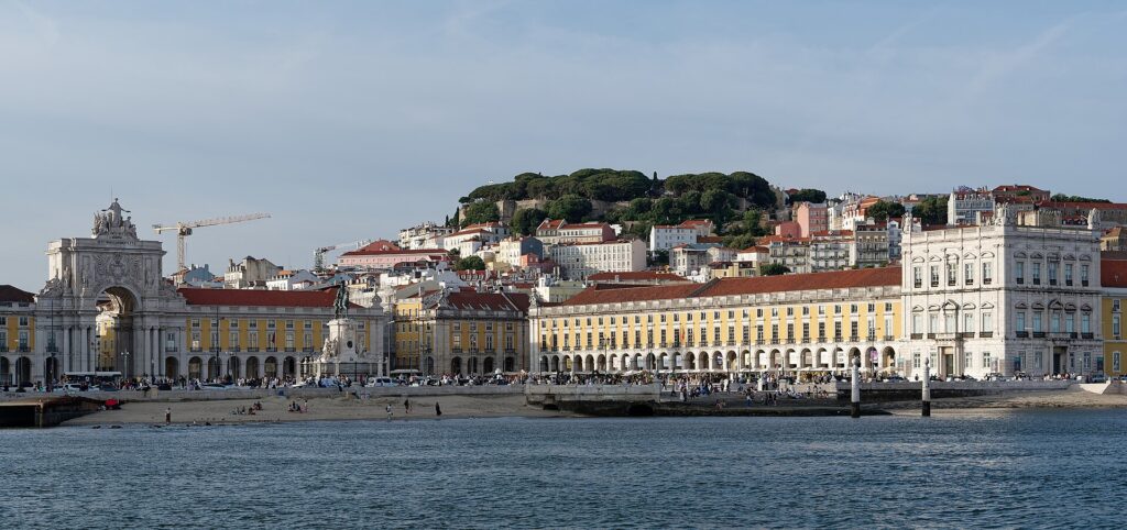 Praça do Comércio's arcades and triumphal arch seen from the Tagus, with São Jorge Castle on the hill above