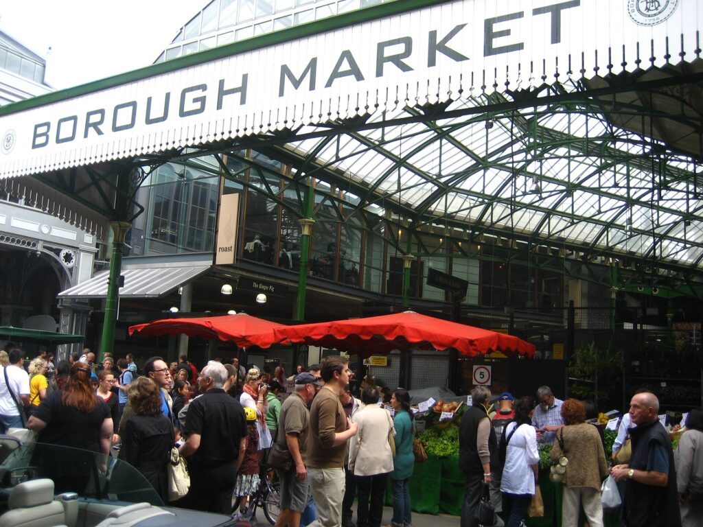 Shoppers under the green iron roof and sign of Borough Market in London