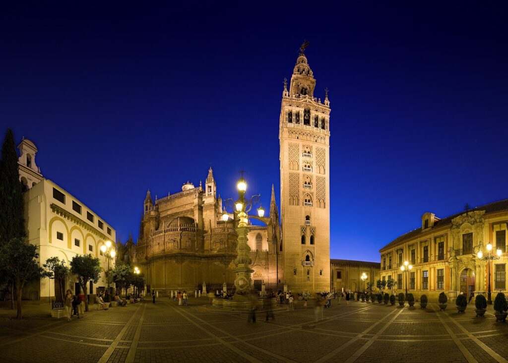 The Giralda bell tower and Seville Cathedral lit up at night above Plaza Virgen de los Reyes